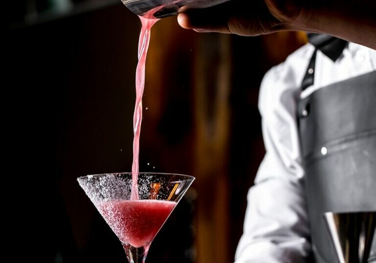 bar tender pours cocktail from cocktail shaker into martini glass