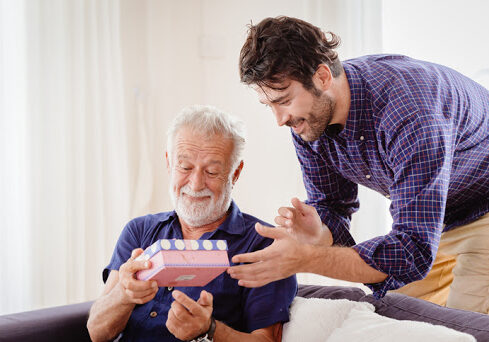 elder happy greeting with gift box present from his son sitting in living room.