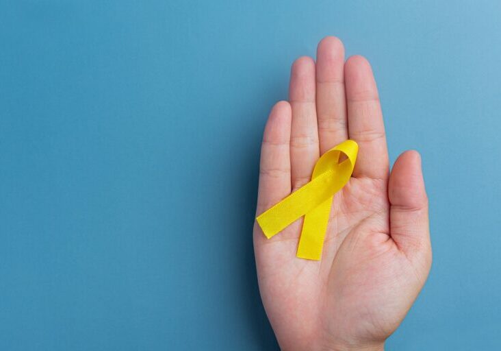 Hands holding yellow ribbon, symbol of cancer awareness, medical support and prevention with helping hand. Suicide prevention day concept