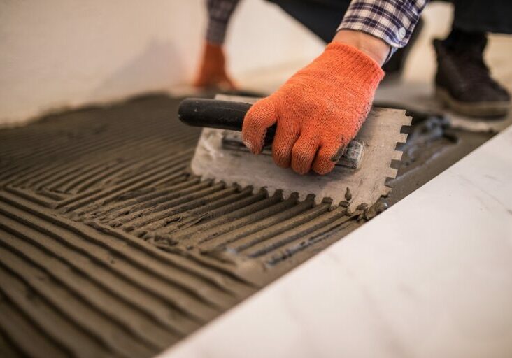 Troweling mortar onto a concrete floor in preparation for laying white floor tile.