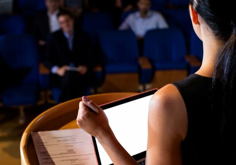 Rear view of female business executive giving a speech at conference center