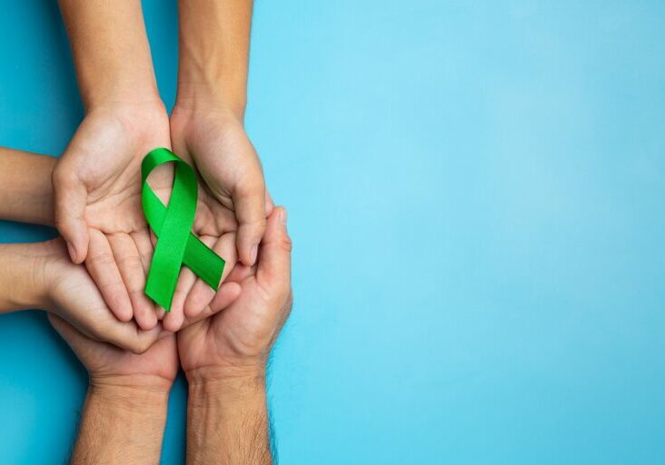 World Mental Health Day; green ribbon put in human's hands on blue background